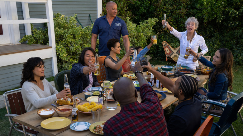 Michelle Rodriguez as Letty, Sung Kang as Han, Nathalie Emmanuel as Ramsey, Vin Diesel as Dom, Leo Abelo Perry as Brian, Rita Moreno as Abuelita, and more having a toast during an outdoor picnic in Fast X