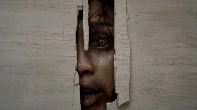 A demonically possessed individual poking their face through a hole in a wall in Evil Dead Burn