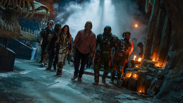 Nicholas Galitzine as Adam walking through a smoky castle room next to Camila Mendes as Teela, Jon Xue Zhang as Ram Man, Christiaan Bettridge as Dian, Idris Elba as Man at Arms, and Johannes Haukur Johannesson as Fisto in Masters of the Universe
