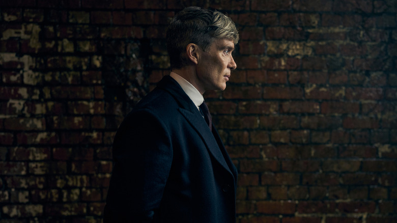 Cillian Murphy as Tommy Shelby walking by a brick wall in Peaky Blinders: The Immortal Man
