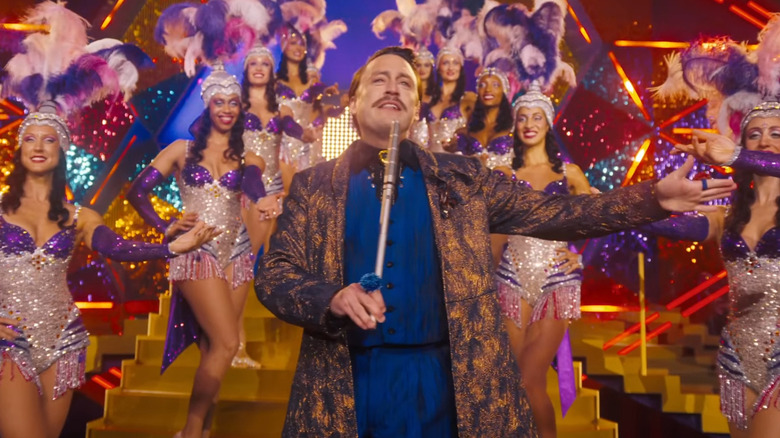 Caesar Flickerman hosting a glitzy show  with showgirls in The Hunger Games: Sunrise on the Reaping