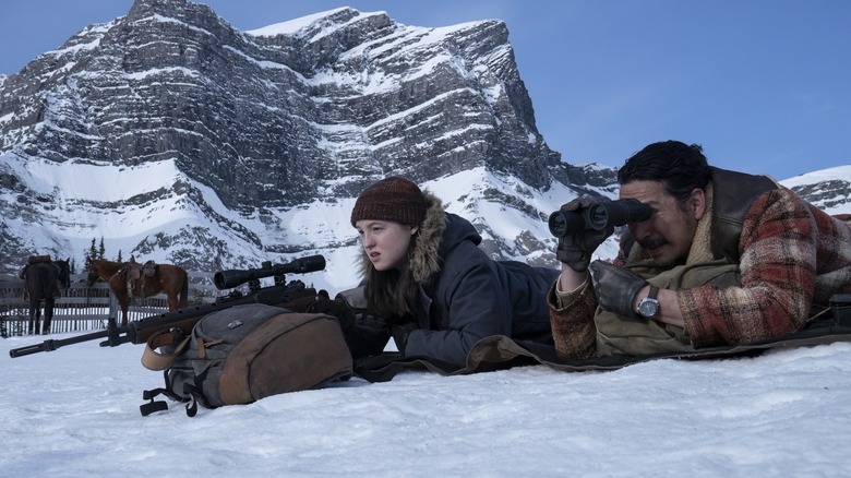 Ellie and Tommy laying in the snow using a scoped rifle in The Last of Us season 2