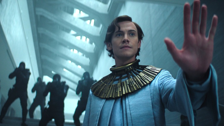 Cassian Bilton as Brother Dawn holding up his hand against a squad of armed guards in Foundation season 3