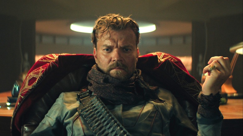 Pilou Asbæk as The Mule seated at a desk with a contemplative look on his face in Foundation season 3