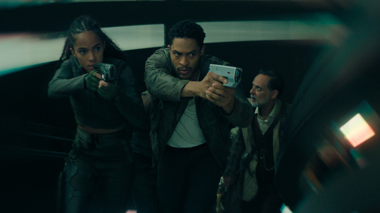 Lou Llobell as Gaal Dornick and Brandon Bell as Han Pritcher brandishing weapons on a staircase as Alexander Siddig as Ebling Mis follows behind in Foundation season 3
