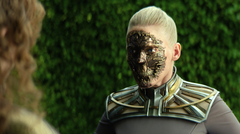 Laura Birn as Demerzel with its robot face exposed standing in front of greenery in Foundation season 3