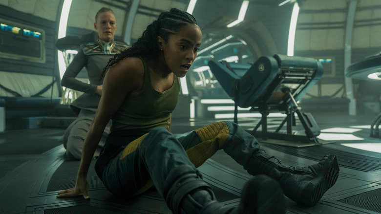 Laura Birn as Demerzel crouching behind Lou Llobell as Gaal Dornick while she appears to be in distress in Foundation season 3