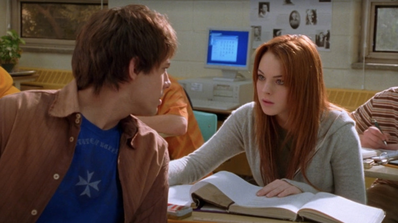 Cady Heron (Lindsay Lohan) sonríe soñadoramente a Aaron Samuels (Jonathan Bennett) que se da la vuelta para mirarla mientras está sentada en sus escritorios de su aula en una escena de Girls Mean