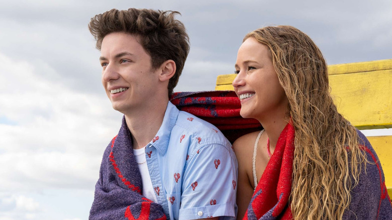 Andrew Barth Feldman and Jennifer Lawrence as Percy and Maddie sharing a towel on a cloudy beach in No Hard Feelings