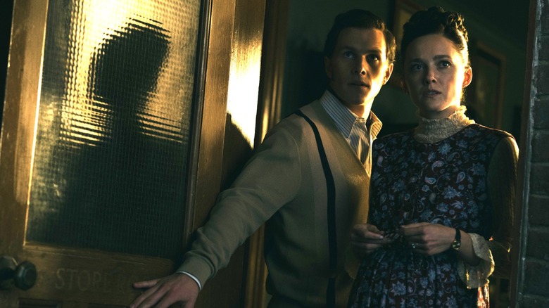 Madison Lawlor as a young Lorraine Warren and Orion Smith as a young Ed Warren standing by an open doorway in The Conjuring: Last Rites