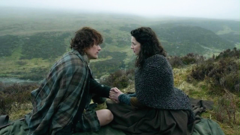 Sam Heughan as Jamie sitting on a hillside with Caitríona Balfe as Claire on Outlander