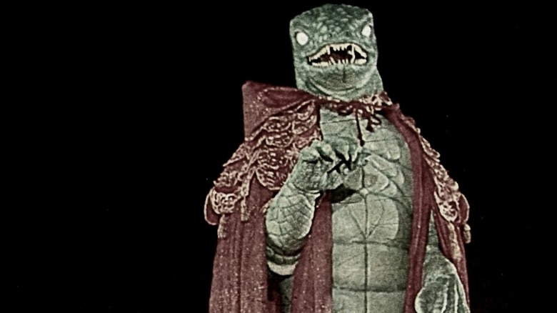 A man in a caped lizard suit approaches in Spectre