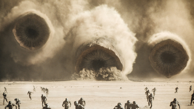 Three enormous sandworms burst out of the desert in front of a fleeing army in Dune: Part Two