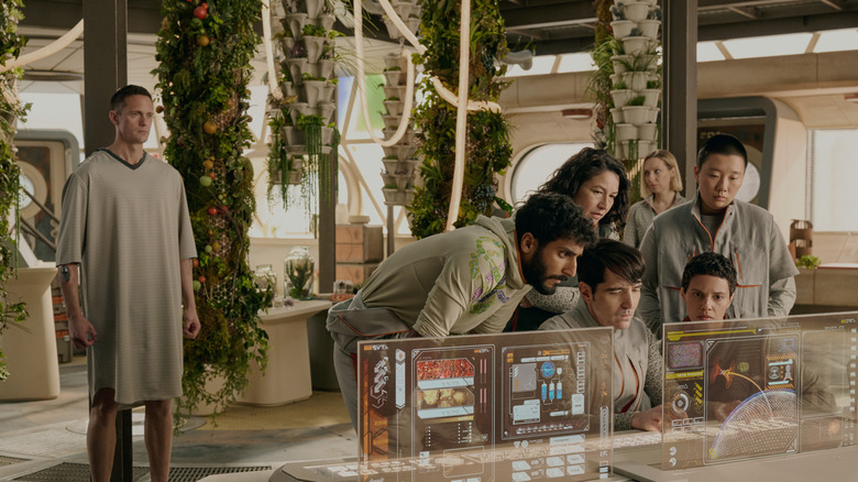 Alexander Skarsgård as Murderbot looking awkward while Akshay Khanna, Tamara Podemski, Anna Konkle, Sabrina Wu, Tattiawna Jones and David Dastmalchian gather around a monitor in Murderbot
