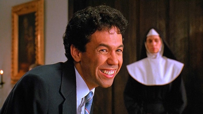 a man in a suit smiling wide in the foreground and a nun in a habit in the background