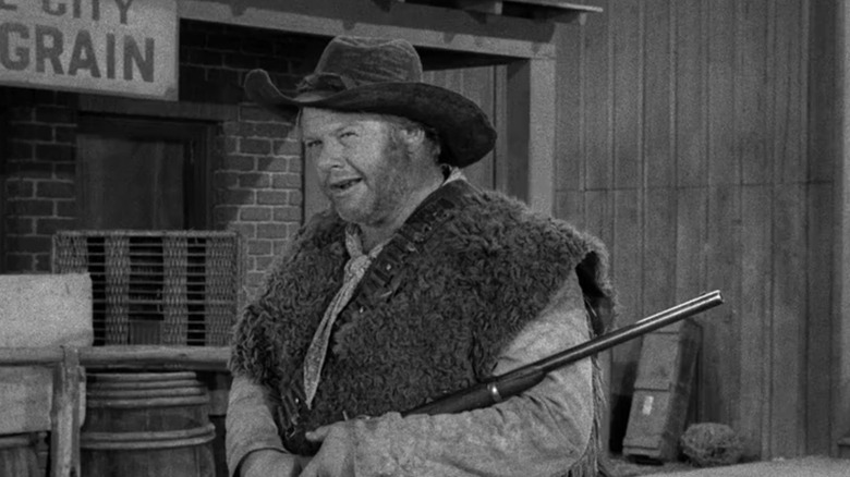 Alan Hale Jr's Jake Higgins stands in the street with a rifle in Gunsmoke