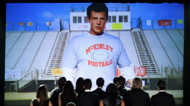 The cast of glee observe a projection of Cory Monteith as Finn Hudson as the character's funeral