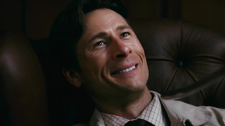 Glen Powell as Becket Redfellow grinning while lying on a couch in How to Make a Killing