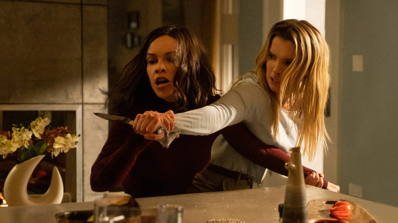 Athena (Hilary Swank) grabs Crystal's (Betty Gilpin) arm and hand holding a knife, both wearing intense expressions in The Hunt