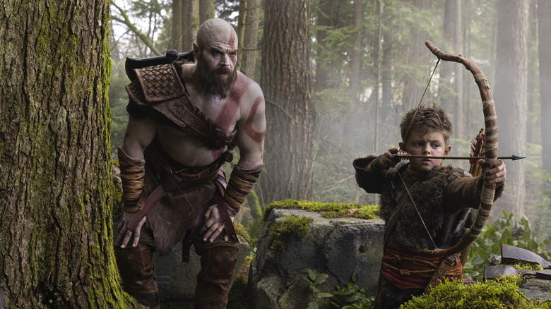 Ryan Hurst dans le rôle de Kratos debout dans une forêt et regardant Callum Vinson dans le rôle d'Atreus tirant un arc et des flèches dans God of War