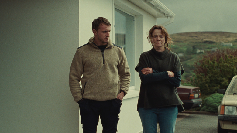 paul mescal and emily watson standing next to each other in a driveway next to a house and two cars in the movie god's creatures
