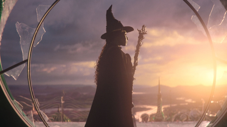 Elphaba holding her broom and looking out of a broken window in Wicked