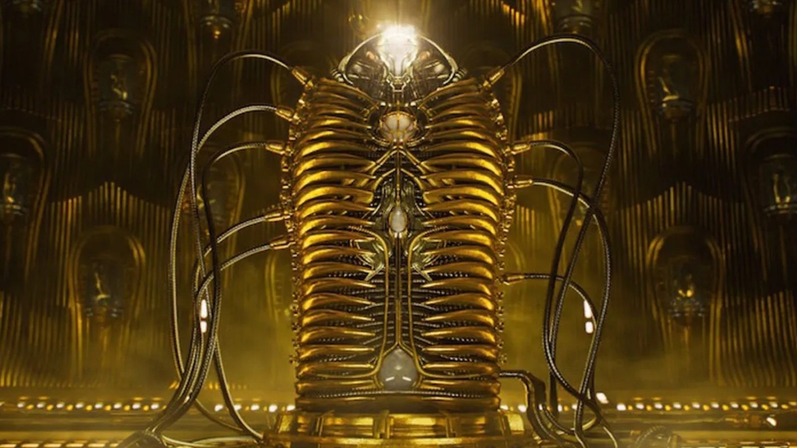A futuristic, golden container (or cocoon) containing Adam Warlock, with numerous cables connected to the cocoon from the ground. In the background stands more golden cocoons. 
