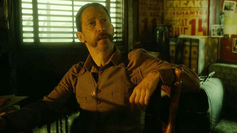 Tim Blake Nelson en tant que Carny Boss (avec une moustache) assis dans Nightmare Alley