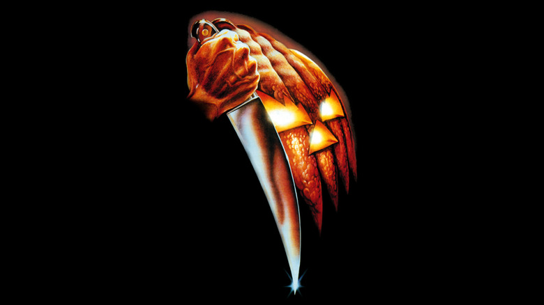 The poster for Halloween (1978) depicting Michael Myers' fist holding a knife next to a jack-o'-lantern