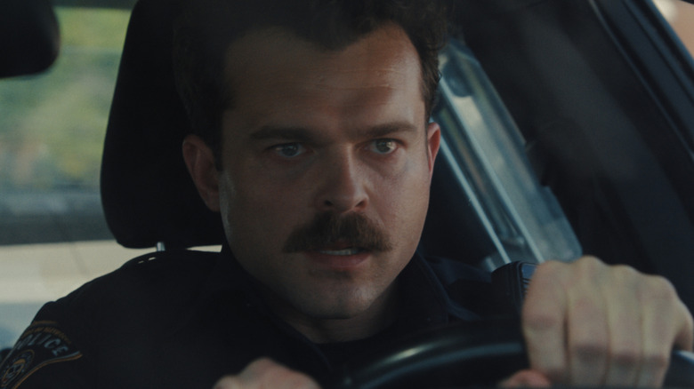 Alden Ehrenreich as Officer Paul behind the wheel of a police car with a serious expression on his face in Weapons
