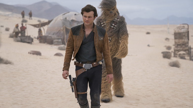 Alden Ehrenreich as Han Solo and Joonas Suotamo as Chewbacca walking through a windy desert camp in Solo: A Star Wars Story