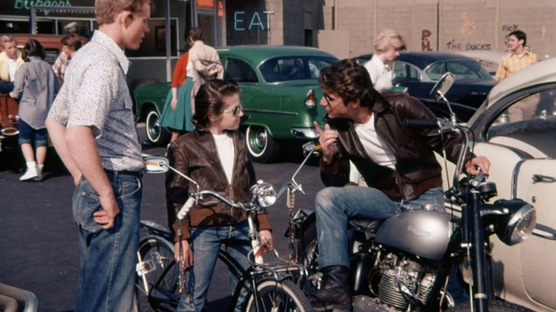 Henry Winkler as Fonzie sitting on a motorbike talking to Ron Howard as Richie Cunningham and a kid in Happy Days