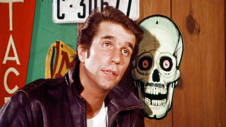 Henry Winkler as Fonzie is seen next to a wall with a skull decoration in Happy Days