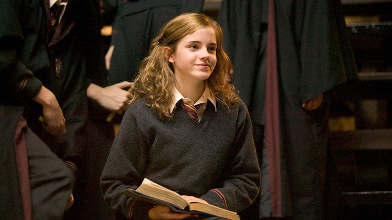Hermione Granger (Emma Watson) smiles while holding an open book in Harry Potter and the Goblet of Fire