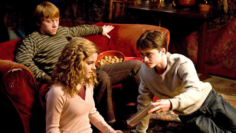 Ron sitting while Harry shows Hermione a book in the Gryffindor common room in Harry Potter and the Half-Blood Prince