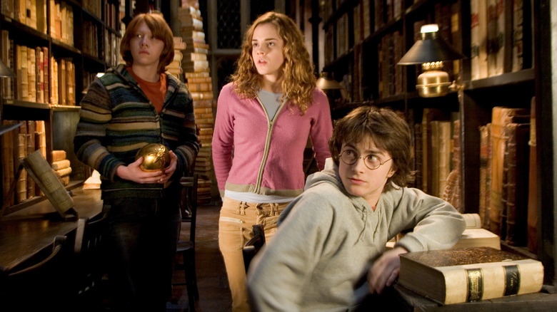 Ron, Hermione, and Harry looking at something in the Hogwarts library in Harry Potter and the Goblet of Fire