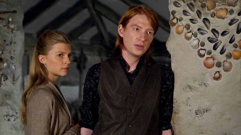 Domhnall Gleeson as Bill Weasley and Clémence Poésy as Fleur Delacour in Harry Potter and the Deathly Hallows: Part 2, standing next to a wall imprinted with seashells and looking at someone out of frame.