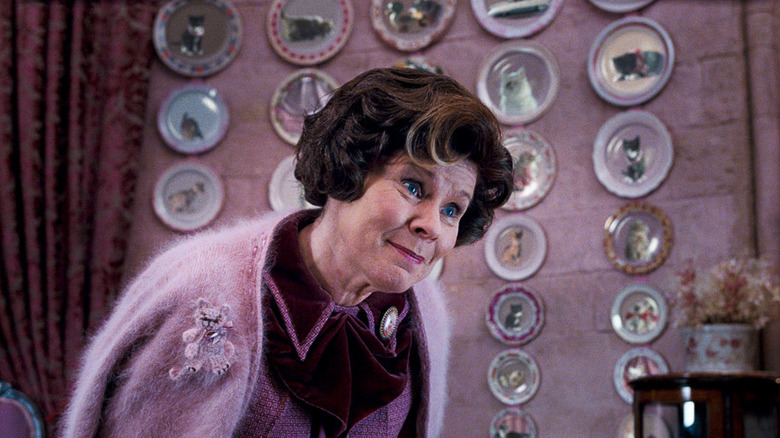 Imelda Staunton as Dolores Umbridge in Harry Potter and the Order of the Phoenix, standing and looking at someone condescendingly against a wall of cat plates.
