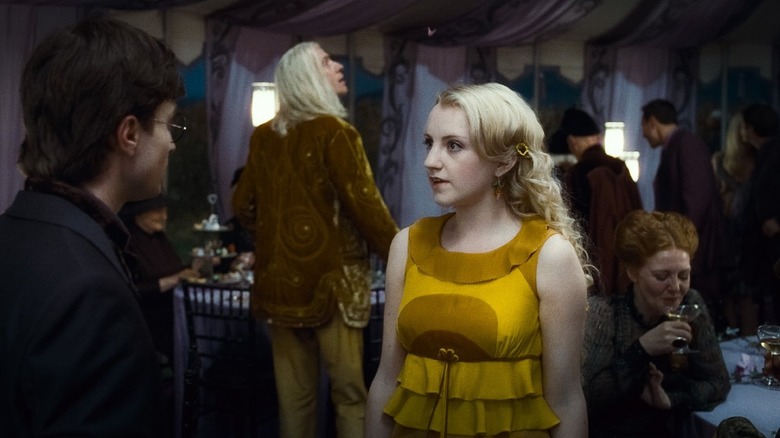 Evanna Lynch as Luna Lovegood standing and talking to Daniel Radcliffe as Harry Potter in a large tent with many other people in Harry Potter and the Deathly Hallows: Part Two.