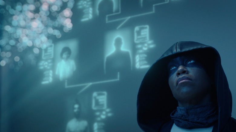 Regina King as Angela Abar wearing hood and black face paint standing in front of blue screen in Watchmen