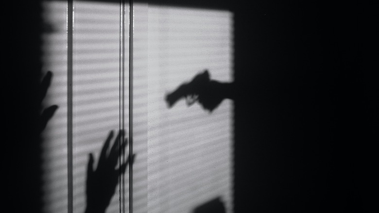Shadow of a gun pointed at someone with their hands up