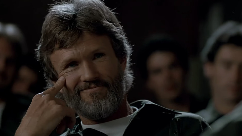 ఫ్లాష్‌పాయింట్‌లోని చీకటి గదిలో కూర్చున్న క్రిస్ క్రిస్టోఫర్సన్ యొక్క బాబీ లోగాన్ క్లోజప్‌లో నవ్వుతున్నాడు