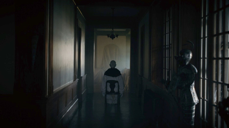 A clown sits in a chair in the Carmichael Manor in Hell House LLC: Lineage