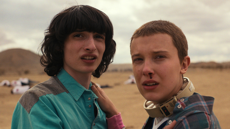 Finn Wolfhard as Mike Wheeler standing next to Millie Bobby Brown as Eleven in the desert in Stranger Things