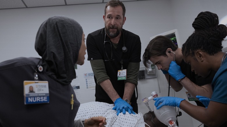Noah Wyle as Michael Robinavitch performing CPR on a patient surrounded by Amielynn Abellera as Perlah Alawi and Patrick Ball as Frank Langdon in The Pitt