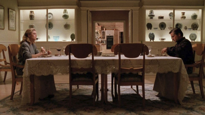 Oliver and Barbara sit at the opposing ends of a long dining room table in The War of the Roses