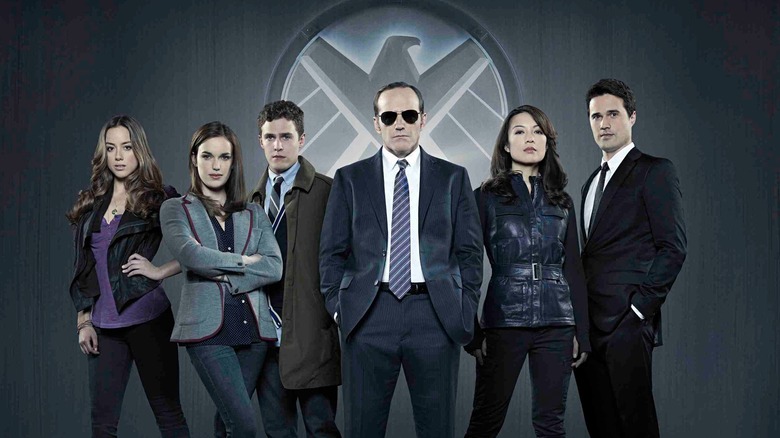 Chloe Bennet, Elizabeth Henstridge, Iain De Caestecker, Clark Gregg, Ming-Na Wen, and Brett Dalton in front of a S.H.I.E.L.D. logo  