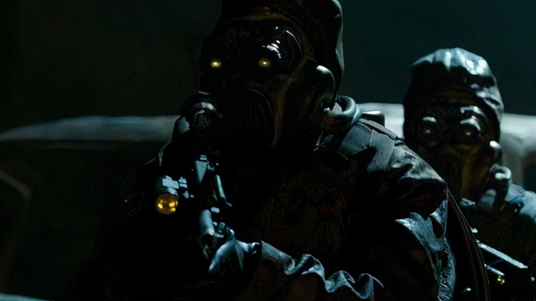 A gas-masked figure with yellow, glowing goggles wearing black tactical gear carries a weapon with a yellow, glowing scope in a dark environment in Hidden