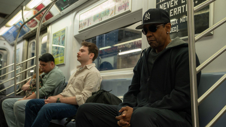 David King wears a hat and sunglasses while sitting on the train in Highest 2 Lowest