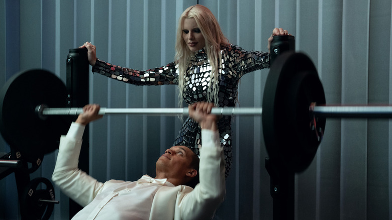 Cam lifts weights in a tuxedo while Elsie watches in Him